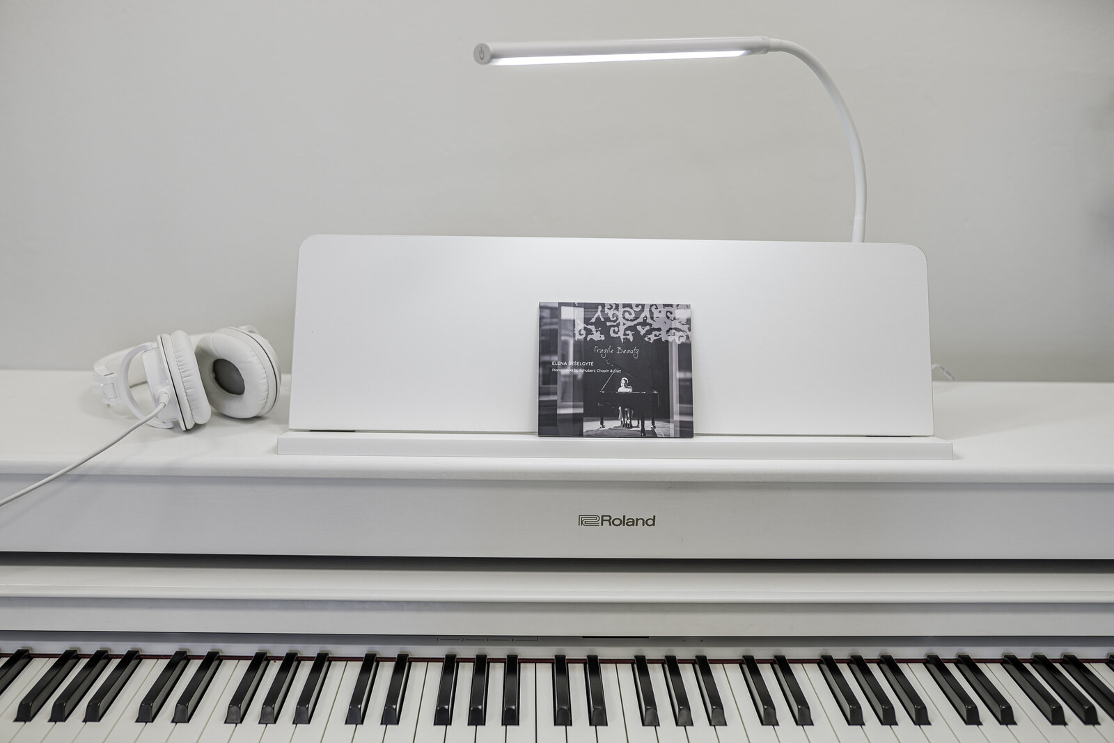 A digital piano at the studio, with headphones and a CD resting on the music stand